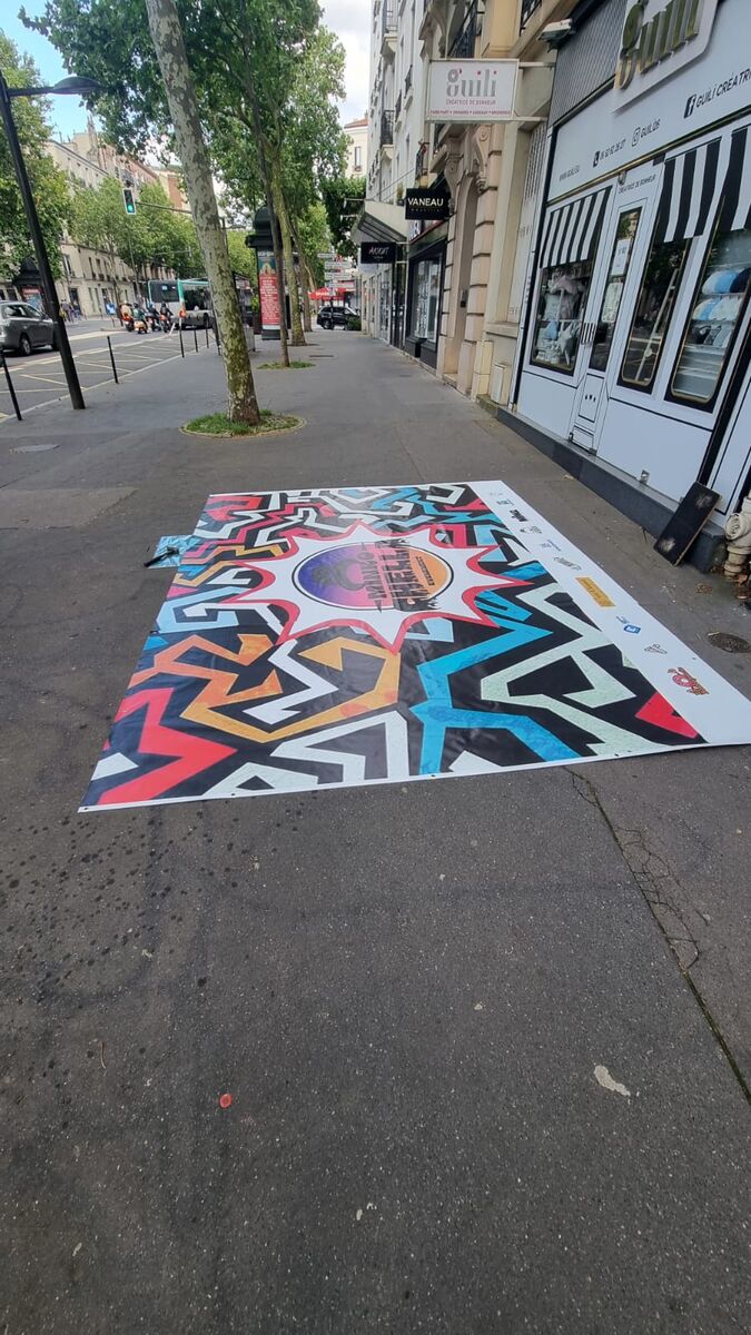 Grande bâche imprimée Minko Chella étalée sur un trottoir — DPS Boulogne